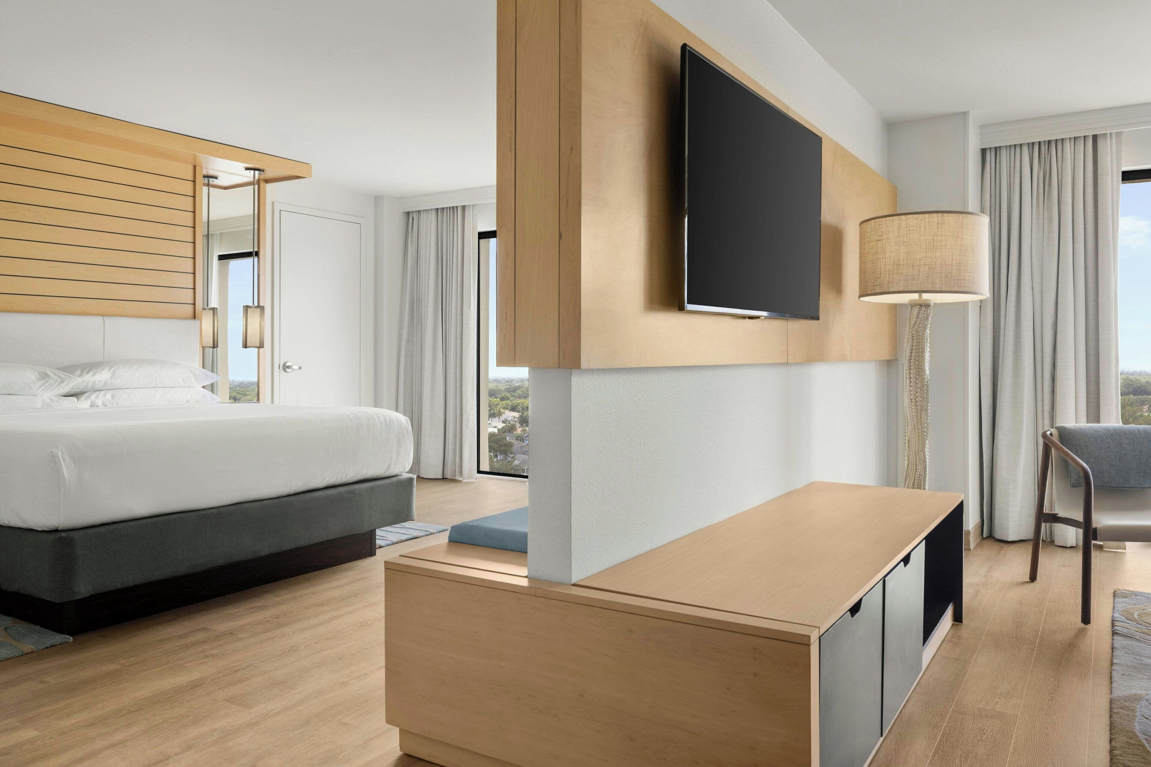 Une chambre d’hôtel moderne équipée d’un lit, d’un téléviseur à écran plat fixé au mur, d’une table de chevet et offrant une vue sur la ville.