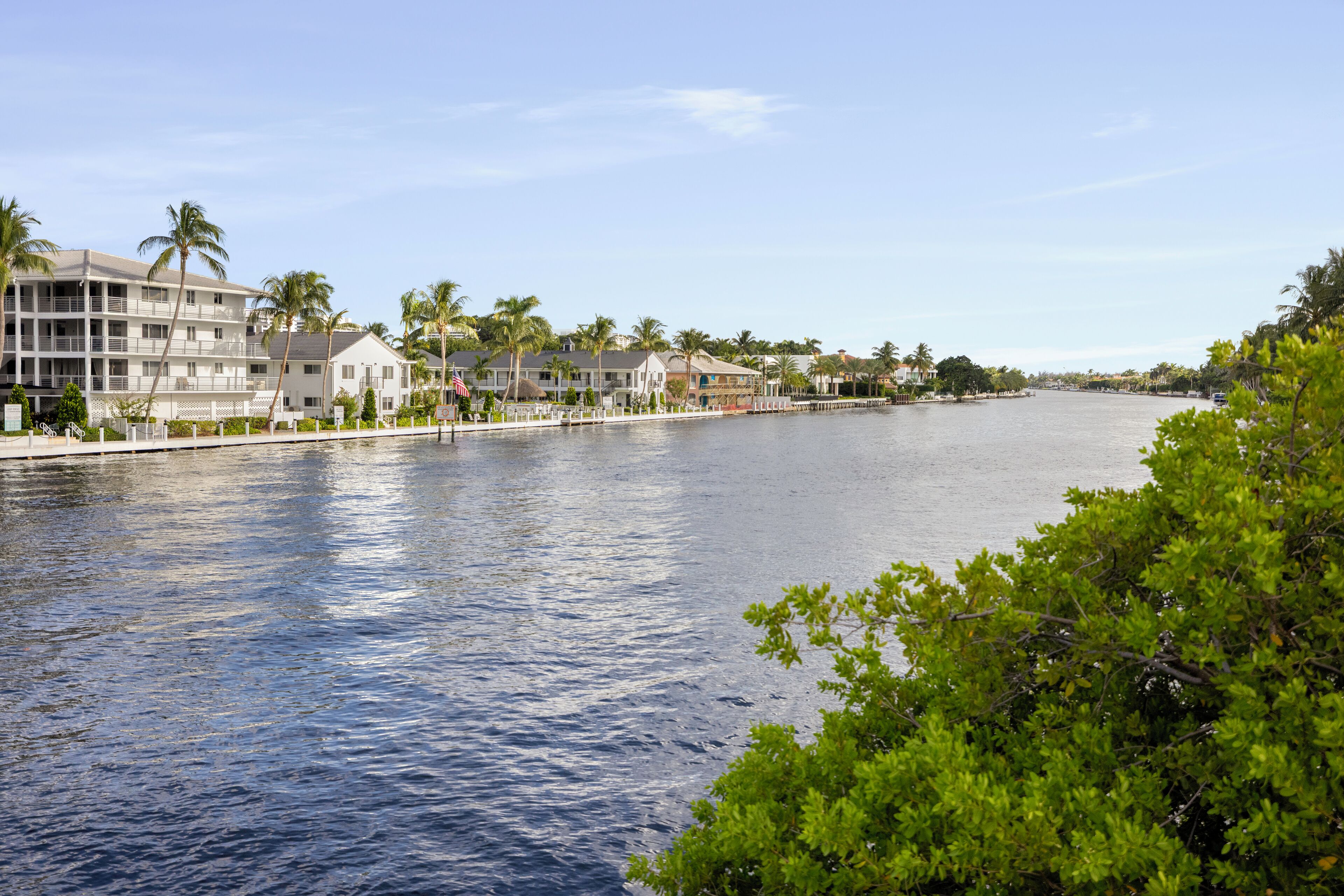 A waterfront hotel with multiple balconies, palm trees, and a clear view of the water.
