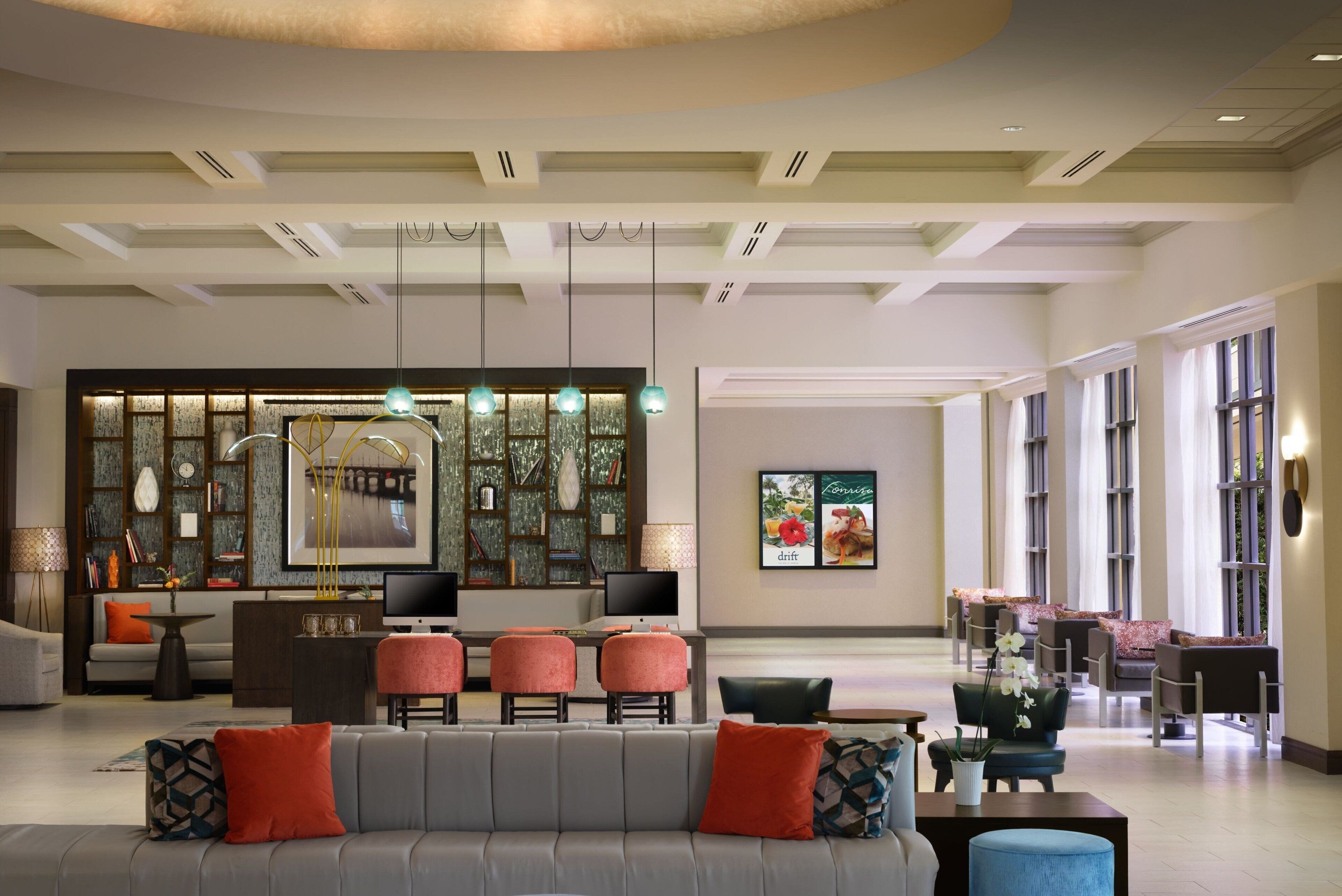 A spacious lobby with a grey sofa, red and blue cushions, a reception desk, and a large window with a city view.