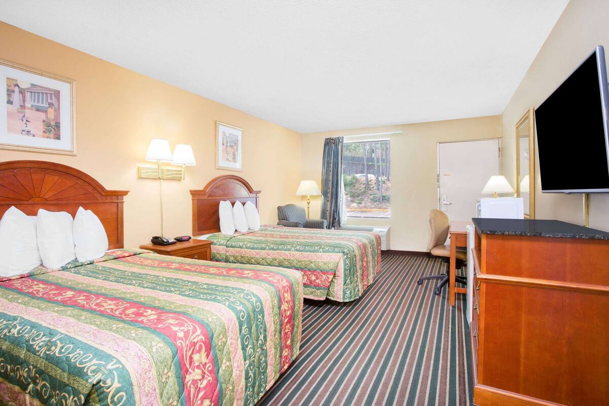 A hotel room with two beds, a desk, a chair, a television, and a window with curtains.