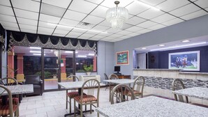 Un restaurante con mesas y sillas de mármol, un candelabro y una pantalla de televisión mostrando un evento deportivo.