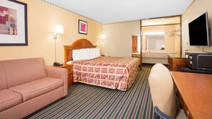 Habitación de hotel con cama, sofá, escritorio con televisor y baño visible a través de una puerta abierta.