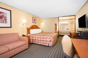 Habitación de hotel con cama, sofá, escritorio con televisor y baño visible a través de una puerta abierta.