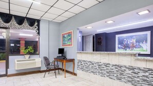 Un área de recepción con suelo de baldosas, un mostrador de recepción, una computadora, una silla y un cuadro grande enmarcado en la pared.