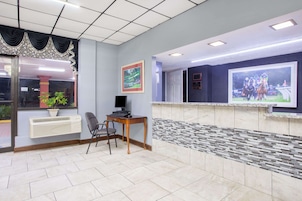 Un área de recepción con suelo de baldosas, un mostrador de recepción, una computadora, una silla y un cuadro grande enmarcado en la pared.