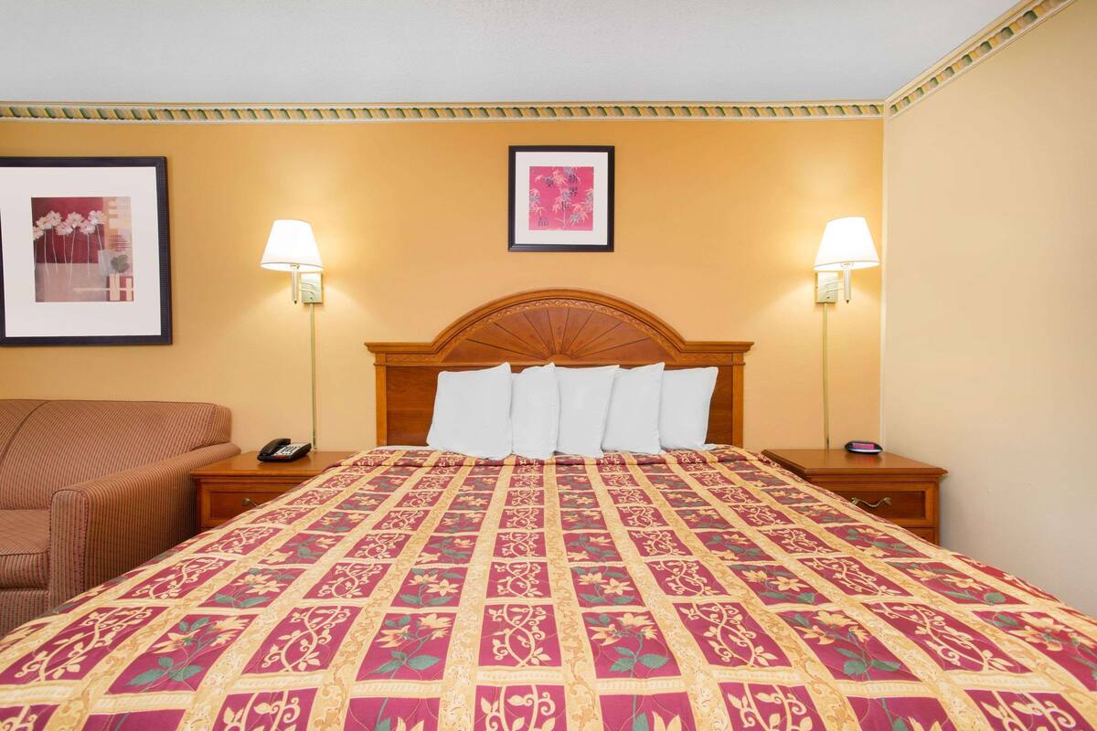 A hotel room with a large bed, two bedside lamps, a wooden headboard, and a framed picture on the wall.