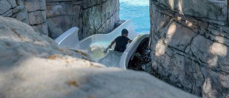 A water slide in a rocky enclosure with a view of the sea.