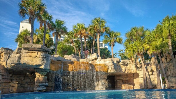 Ein Pool mit Wasserfall, umgeben von Palmen und einer felsigen Landschaft.