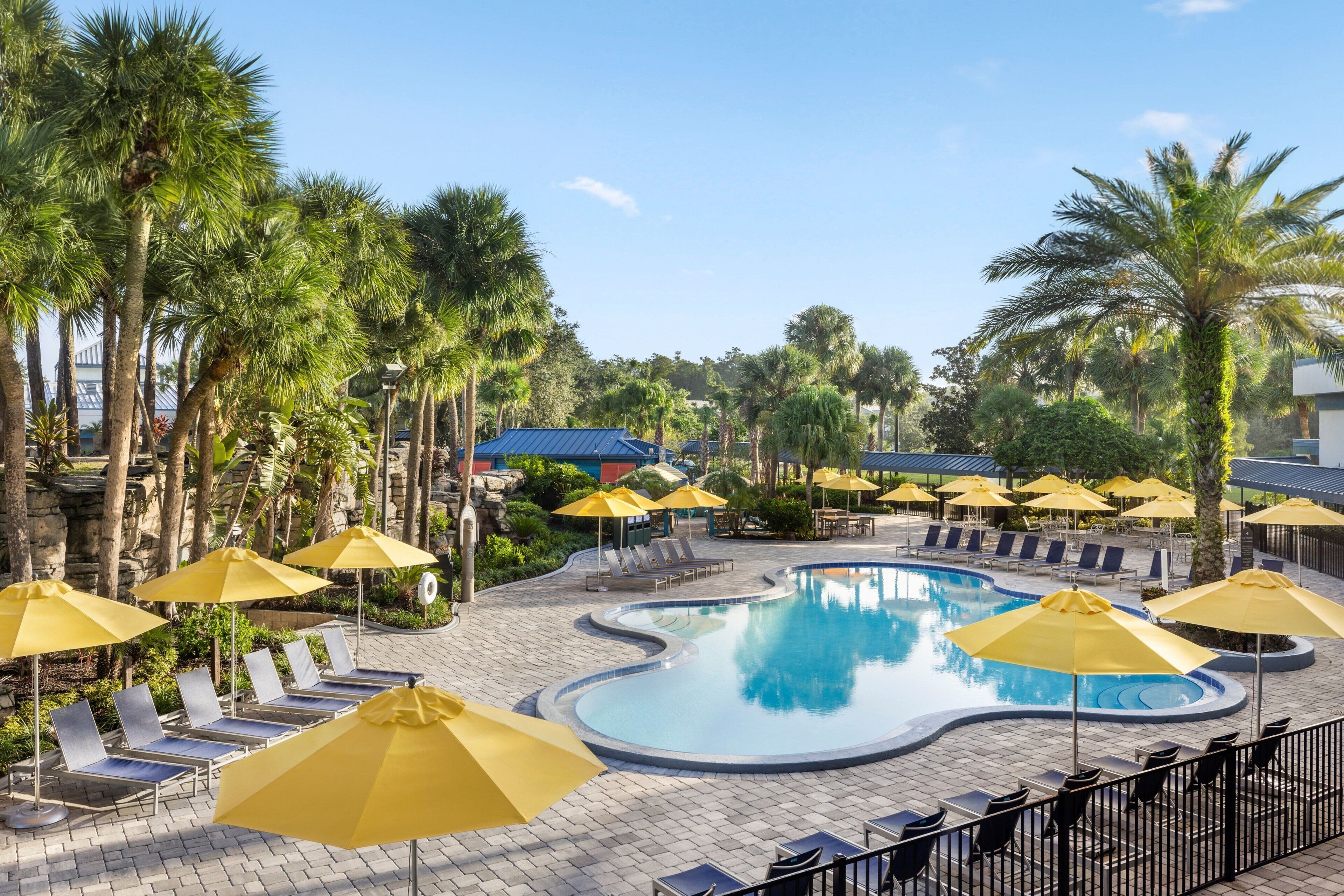 A swimming pool surrounded by palm trees and sun loungers with yellow umbrellas.