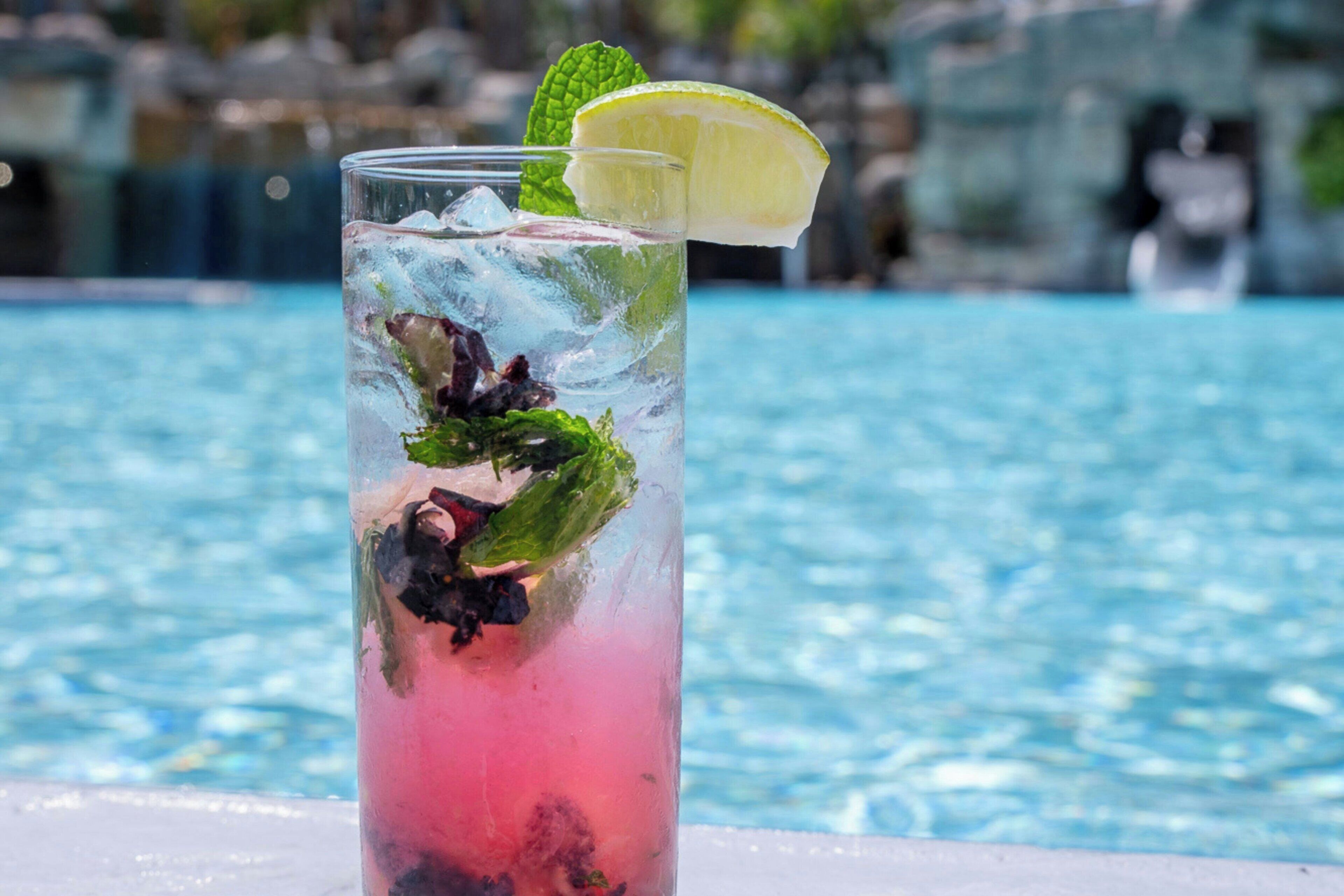 Ein Glas rosa Getränk mit Minze und Limettenscheibe, platziert am Poolrand.