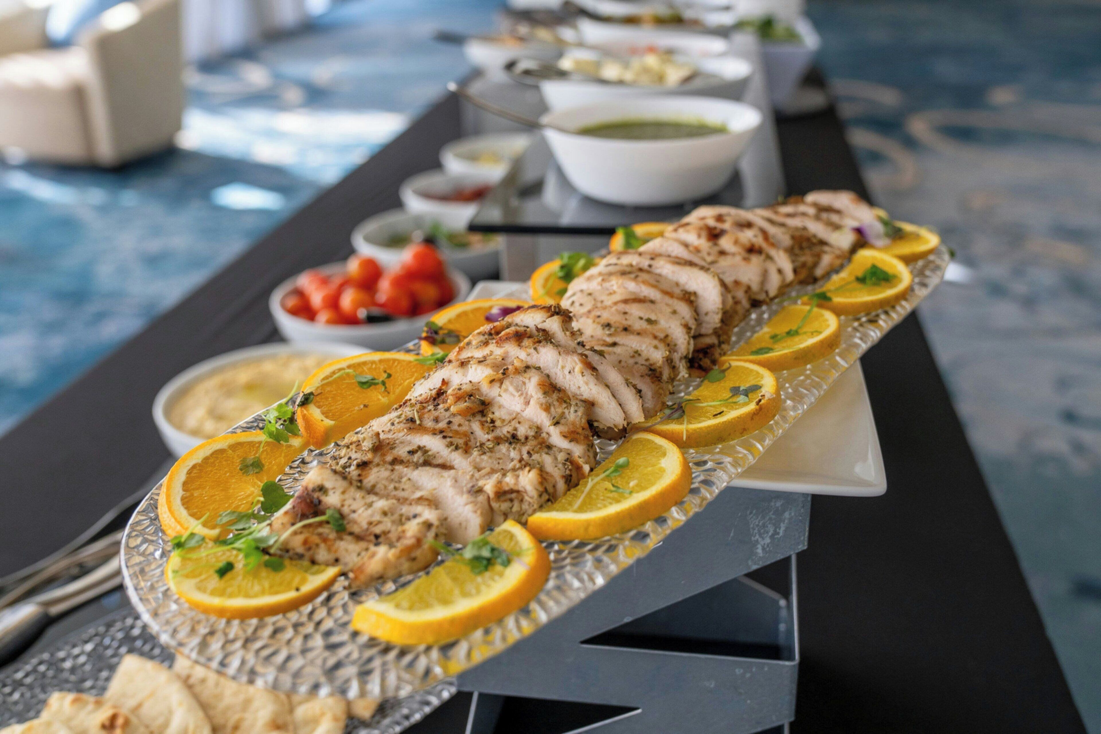 Ein Buffet mit einer großen Platte mit geschnittenem Fleisch, garniert mit Zitronenscheiben und Kräutern.