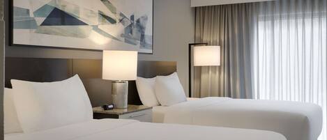 A hotel room with two beds, a large abstract painting, a nightstand with a lamp, and a window with curtains.