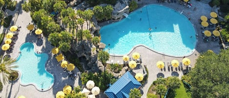 An aerial view of a resort with two swimming pools, sun loungers, and umbrellas.