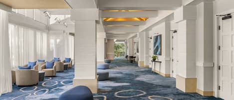 A hotel lobby with a long corridor, seating areas, and a patterned carpet.