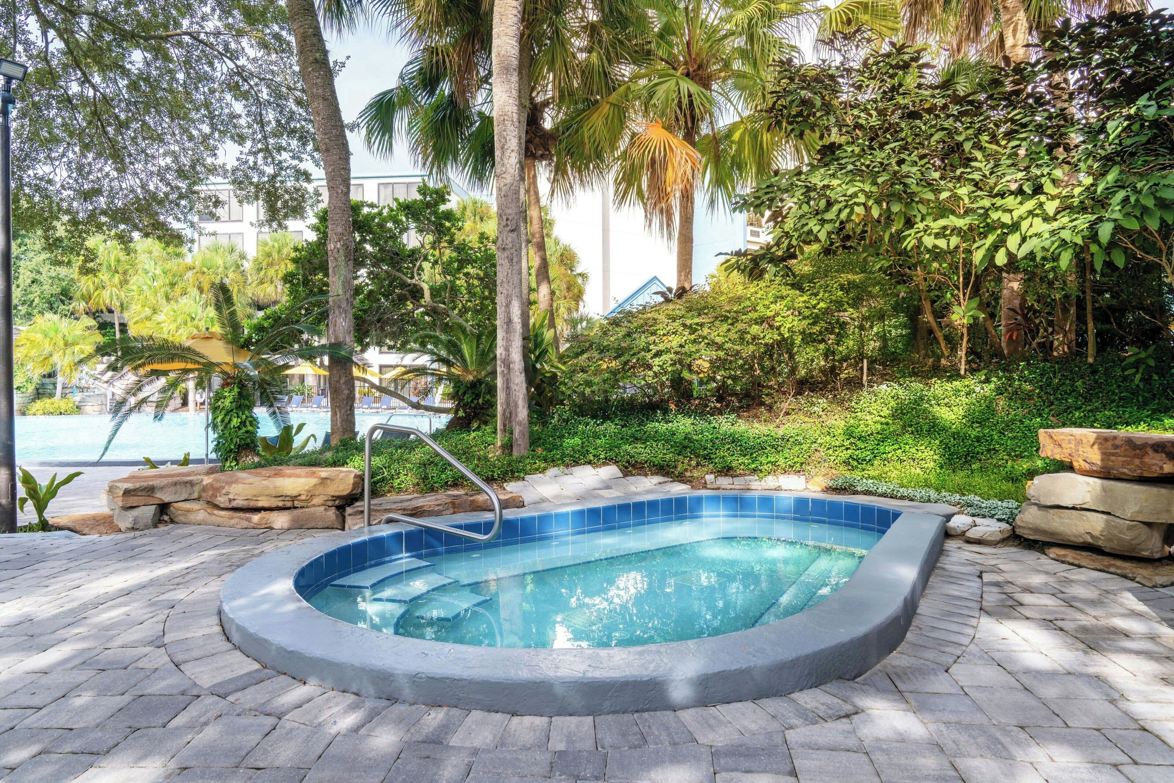 Un jacuzzi rodeado de escalones de piedra y vegetación, con una piscina al fondo.