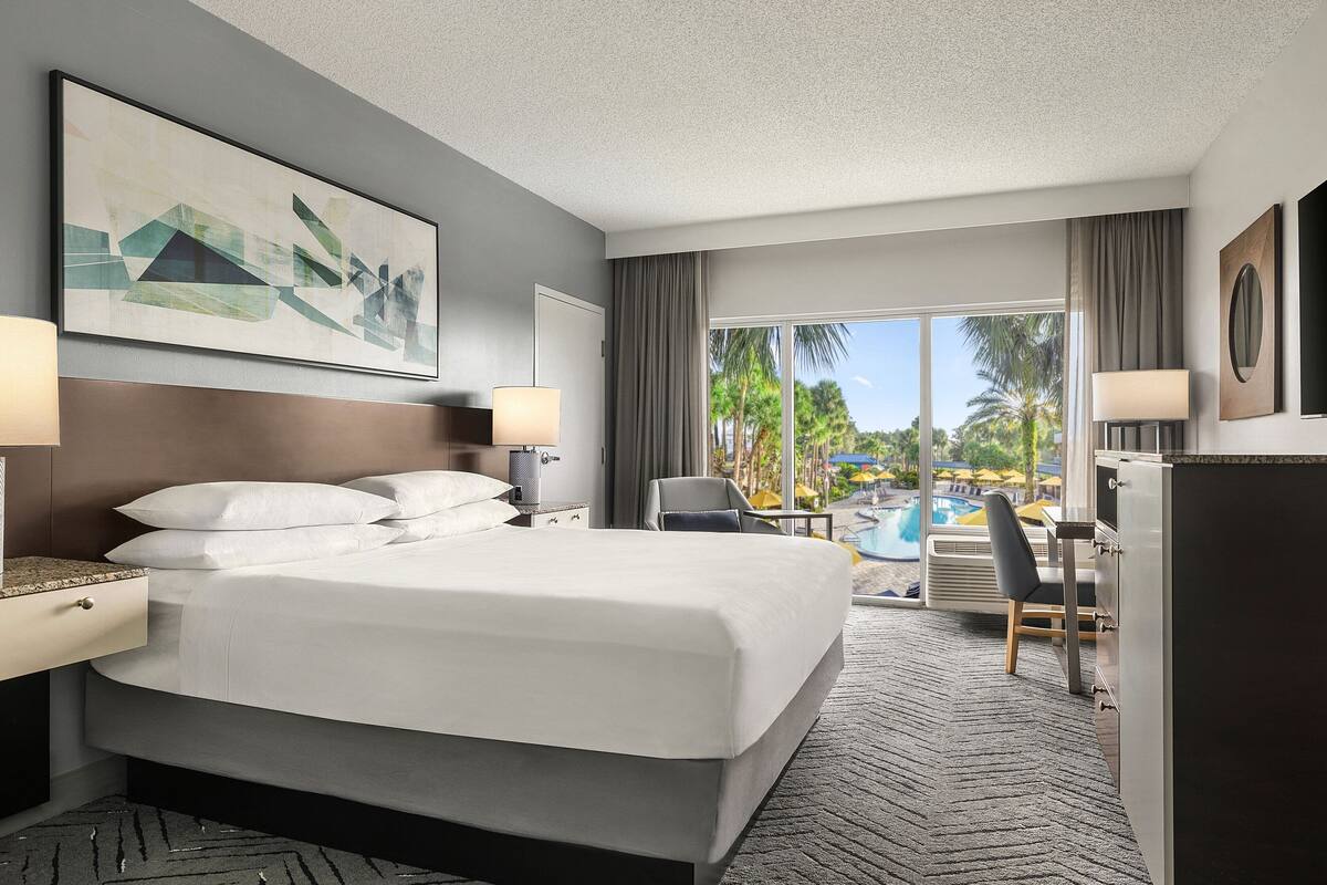 A hotel room with a large bed, a desk, a chair, and a view of a swimming pool.