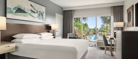 A hotel room with a large bed, a desk, a chair, and a view of a swimming pool.