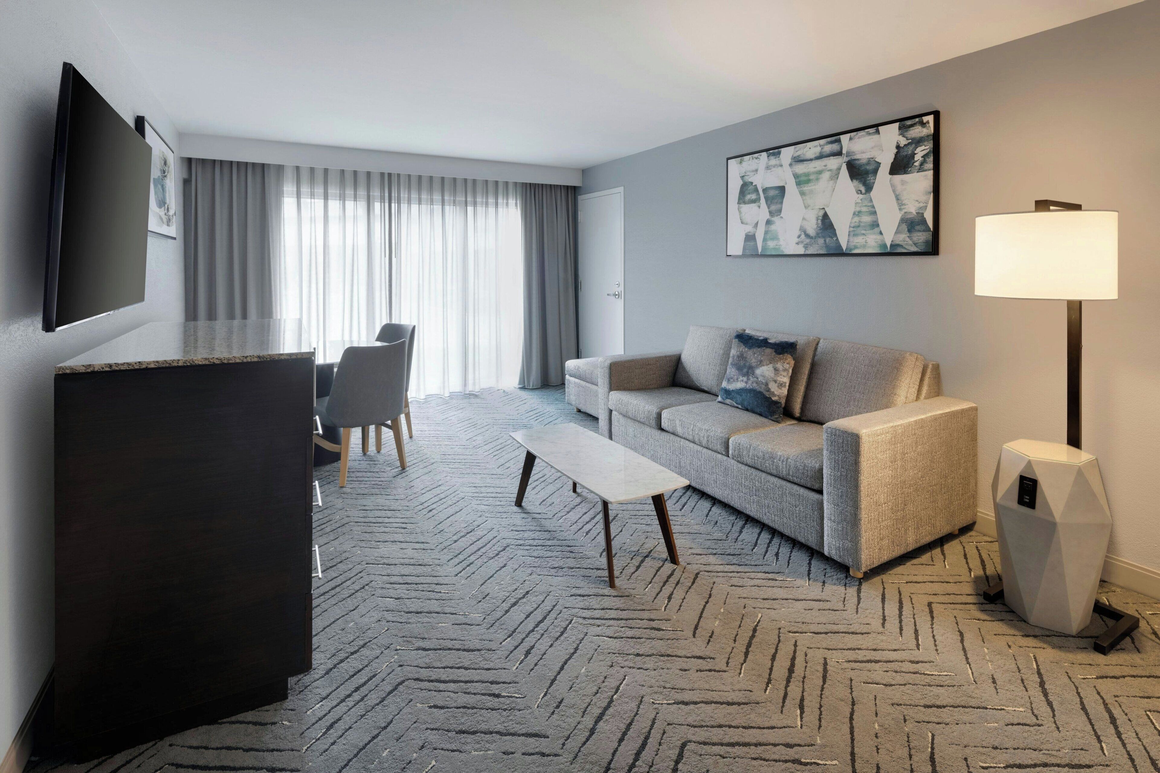 A hotel room with a flat-screen TV, a sofa, a coffee table, a desk, and a lamp.