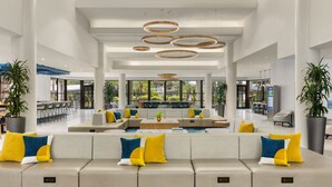 Eine großzügige Lobby mit modernem Design, ausgestattet mit einer geräumigen Sitzecke, Sofas und einem Couchtisch, umgeben von großen Fenstern mit Blick ins Freie.