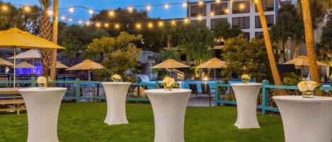 An outdoor setting with white tables, string lights, and umbrellas.