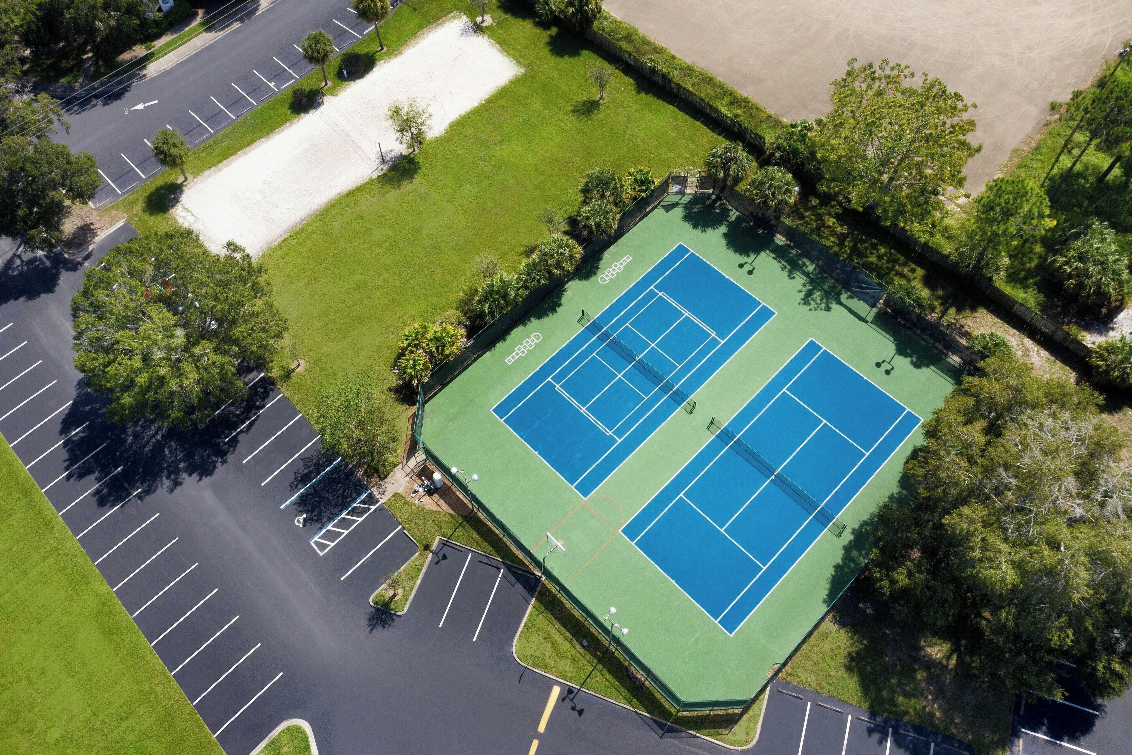 Eine Vogelperspektive auf einen Tennisplatz, umgeben von Parkplätzen und Grünflächen.