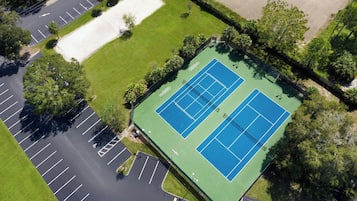 Vista aérea de una cancha de tenis rodeada de espacios de estacionamiento y zonas verdes.