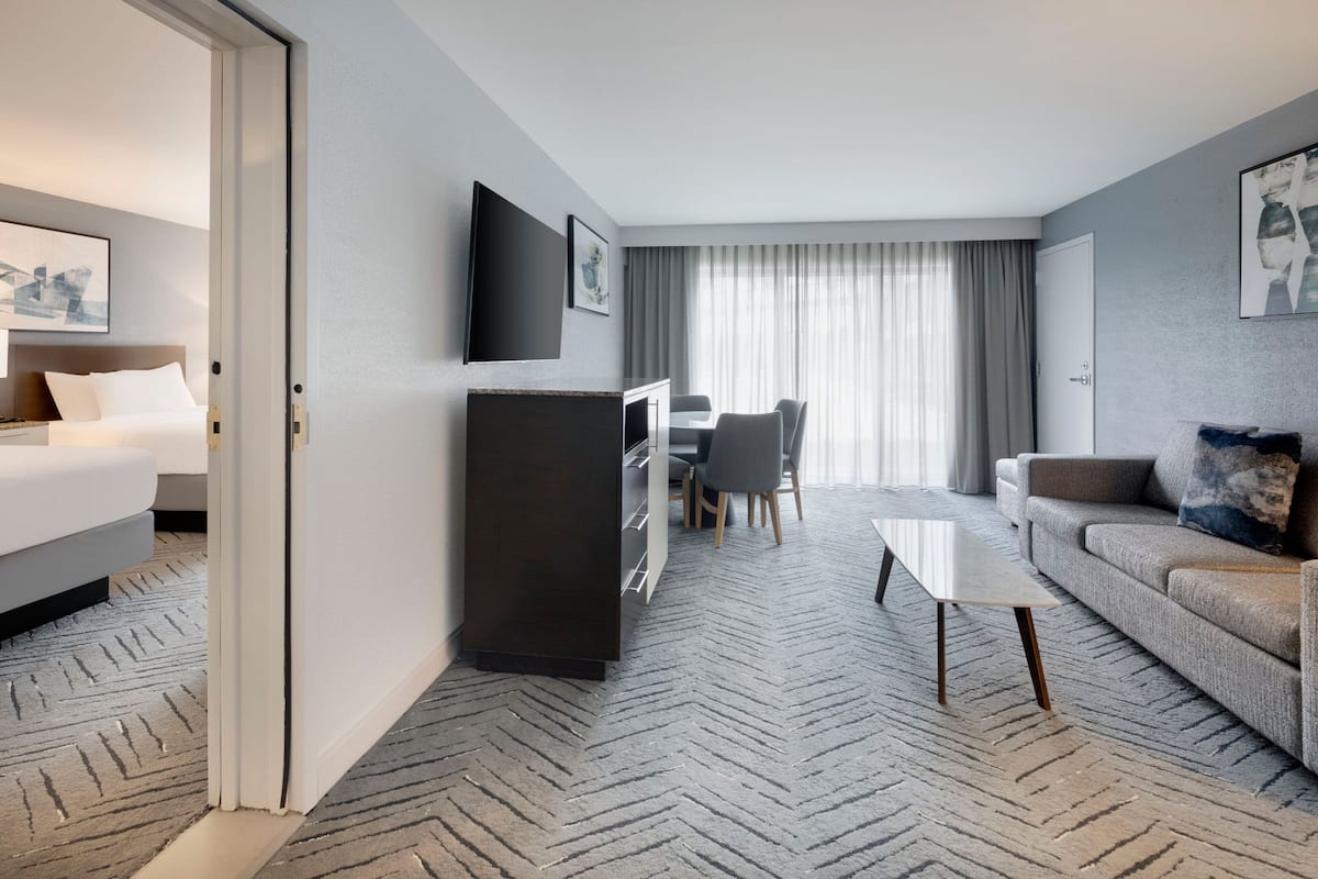 A hotel room with a bed, a desk with a chair, a sofa, a coffee table, and a TV mounted on the wall.