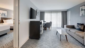 A hotel room with a bed, a desk with a chair, a sofa, a coffee table, and a TV mounted on the wall.