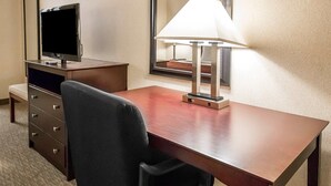 Une chambre d’hôtel avec un bureau en bois, une chaise de bureau noire, une télévision, une lampe et un miroir.