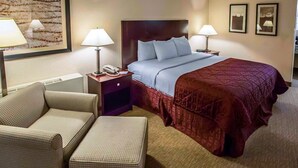 Une chambre d’hôtel avec un lit, deux tables de chevet avec des lampes, une chaise et un tapis à motifs.