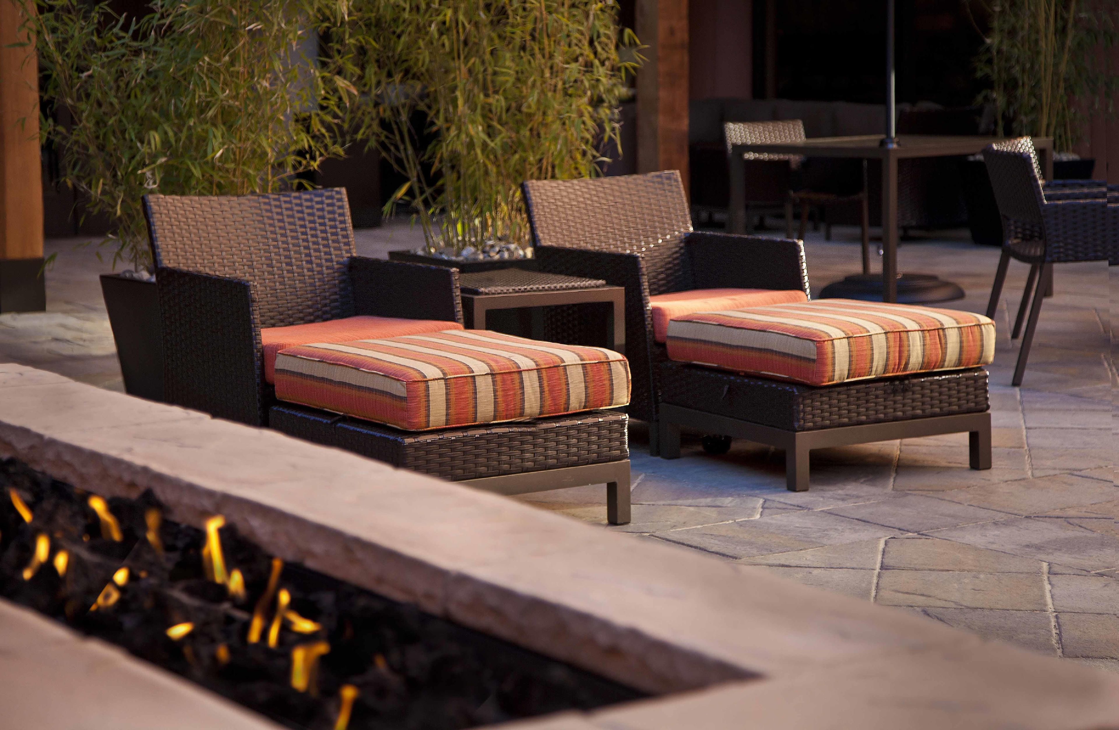 An outdoor seating area with wicker chairs and cushions, a table, and a fire feature.