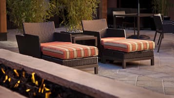 An outdoor seating area with wicker chairs and cushions, a table, and a fire feature.