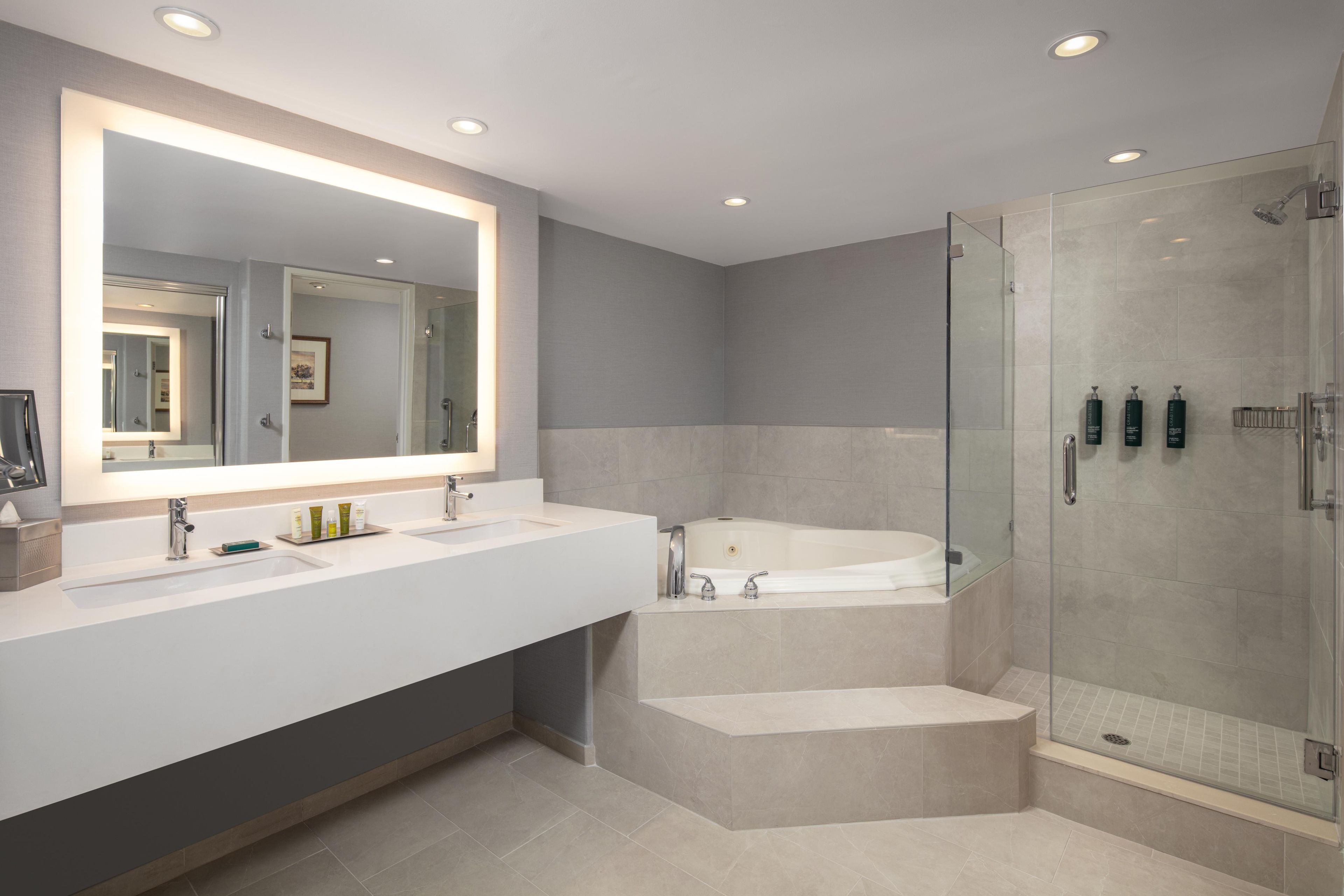A modern bathroom with a large mirror, dual sinks, a glass-enclosed shower, and a bathtub.