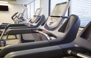 Varias cintas de correr en un gimnasio, con un televisor de pantalla plana en la pared.