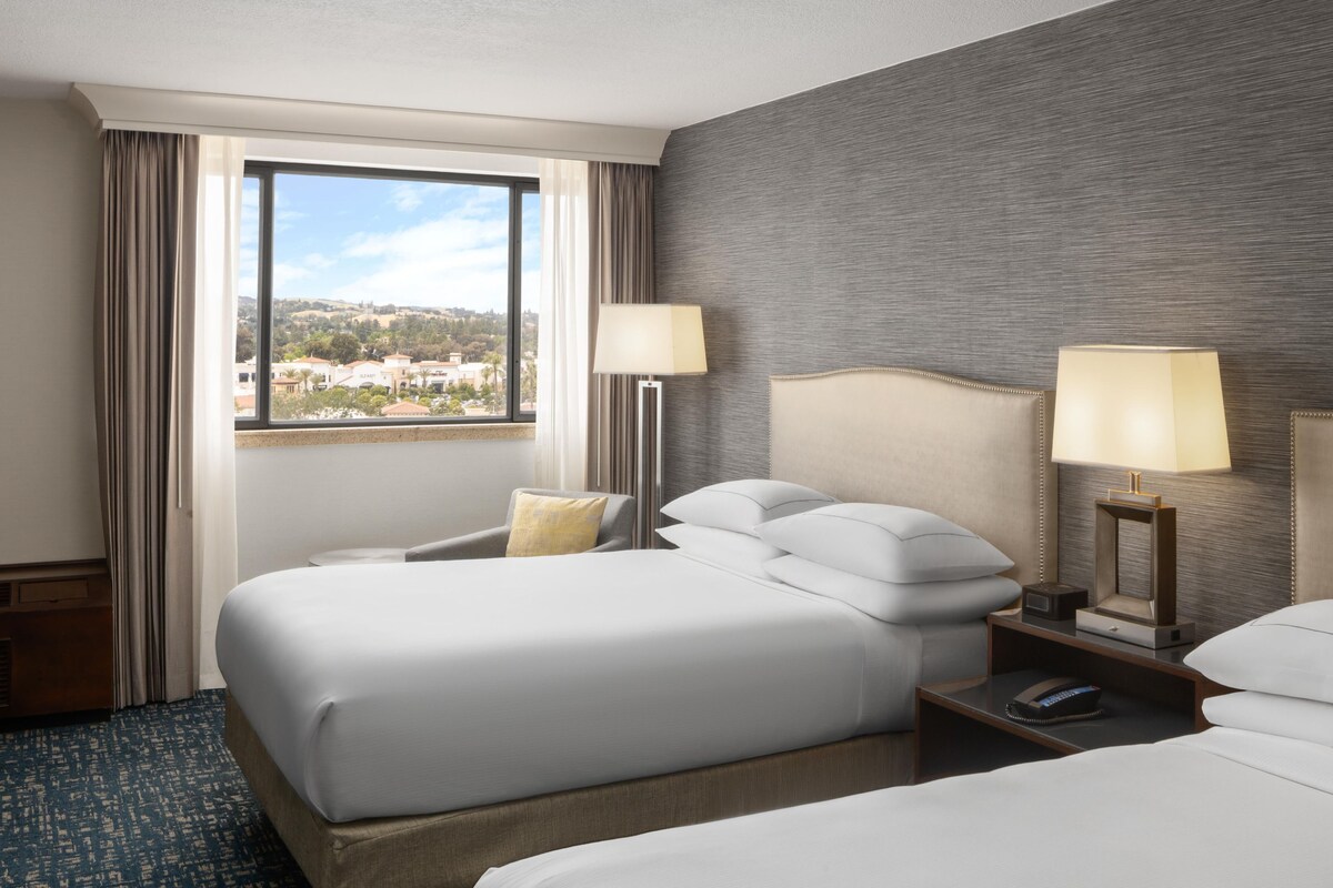Habitación de hotel con dos camas, vista a la ciudad y diseño moderno.