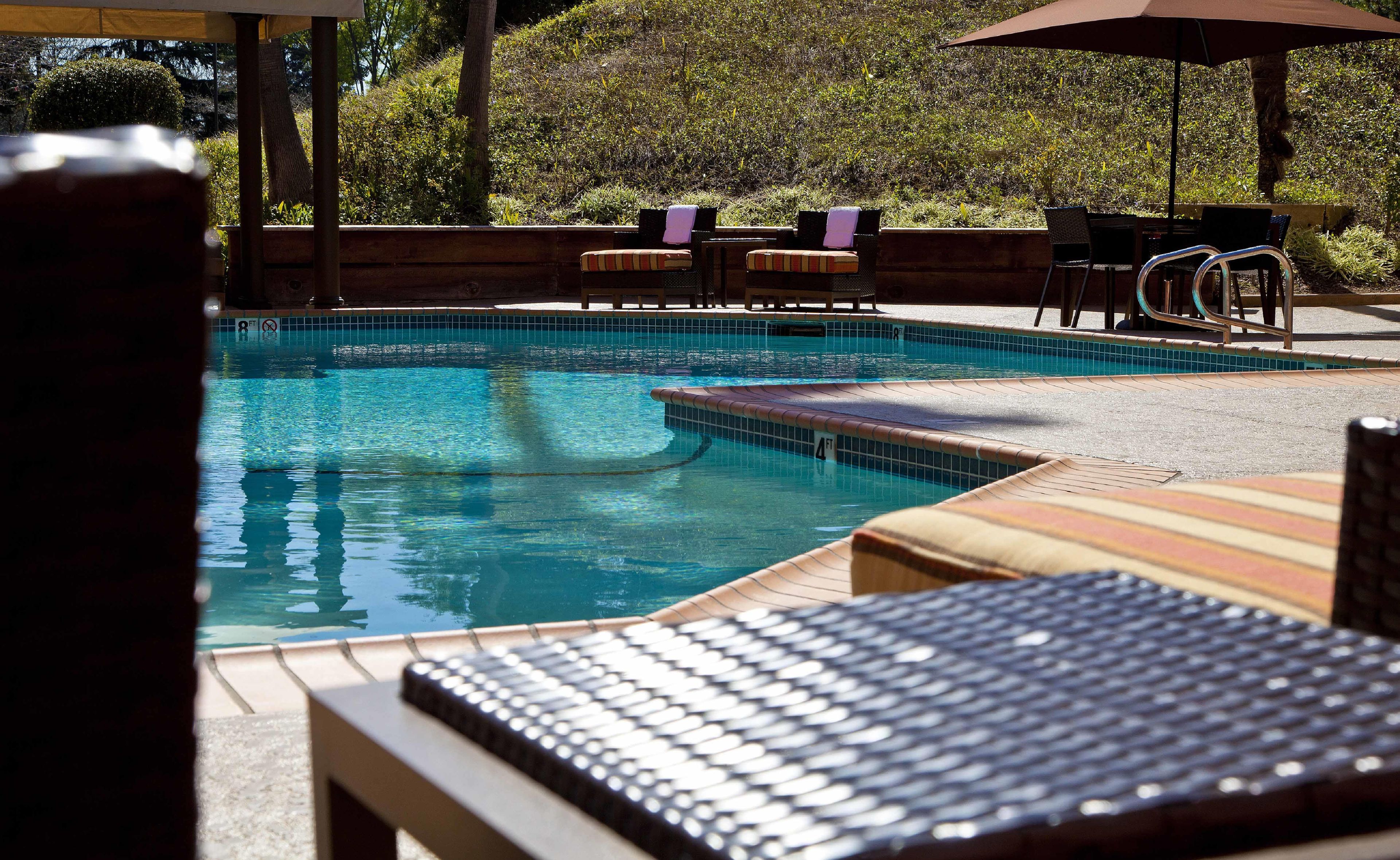 A swimming pool with lounge chairs and umbrellas, surrounded by greenery.