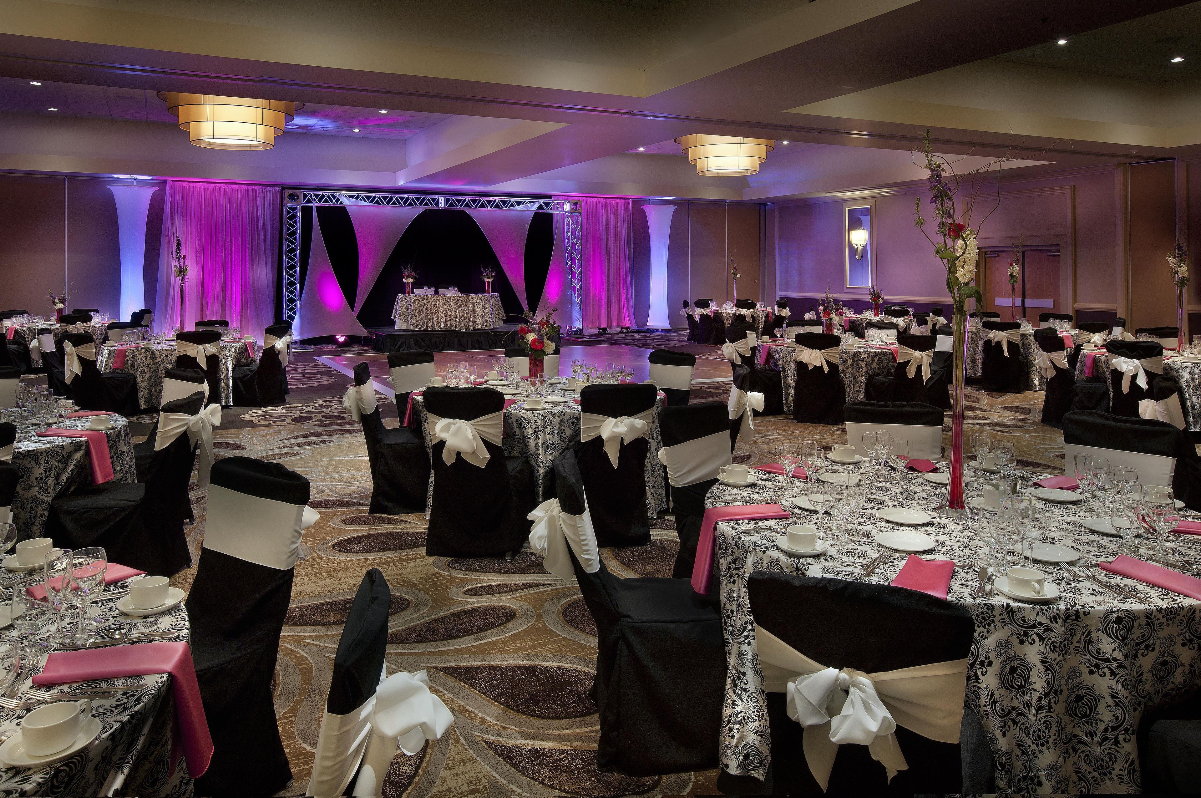 A banquet hall with round tables set for a formal event, featuring a stage and draped curtains in the background.