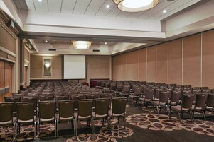 A conference room with rows of chairs, a projector screen, and a carpeted floor.