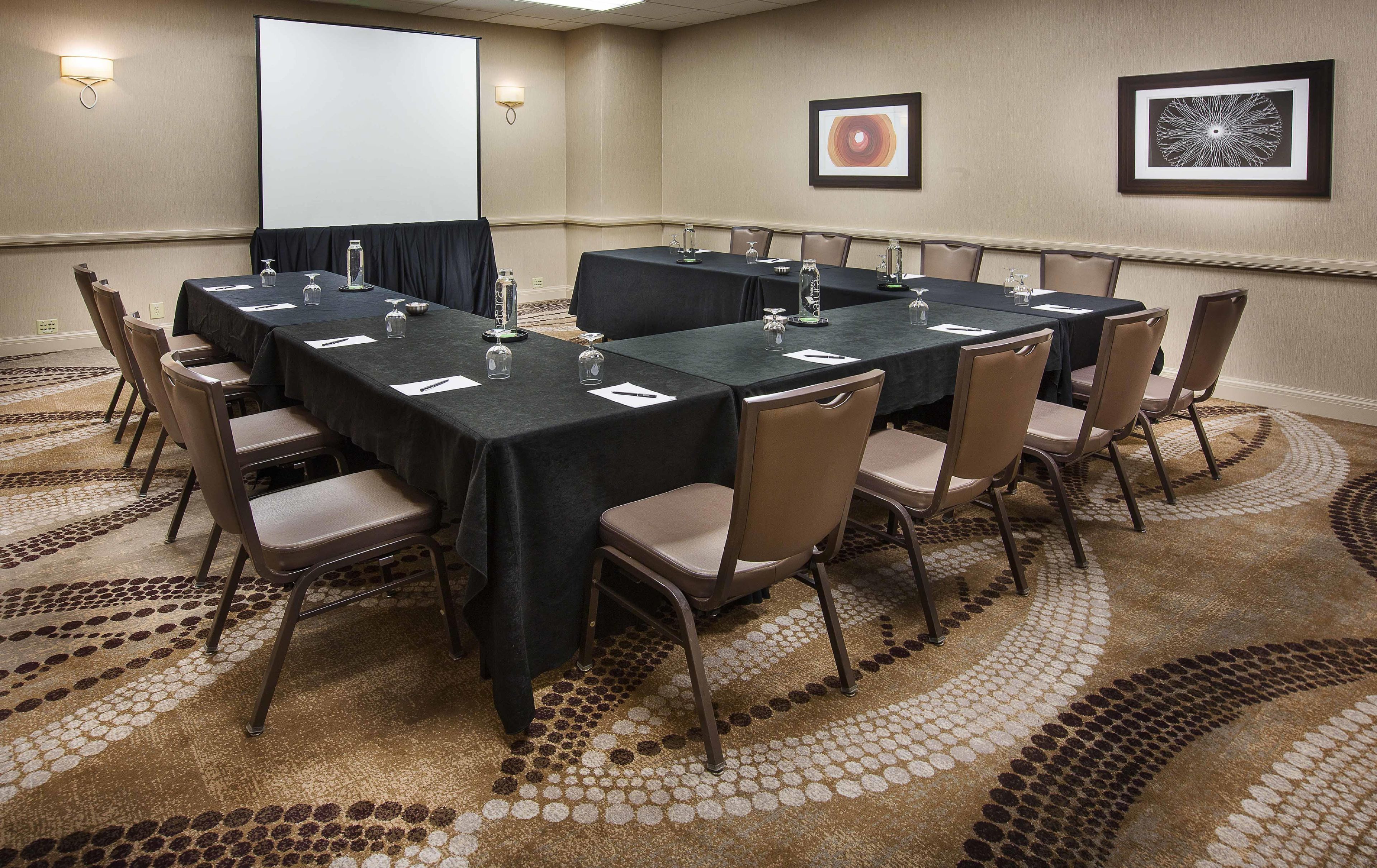 Une salle de conférence équipée d’une grande table, de chaises, d’un écran de projection et d’œuvres d’art encadrées accrochées aux murs.