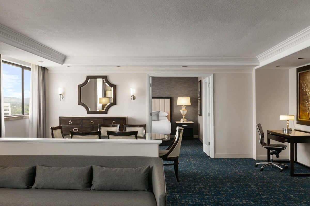 Una habitación de hotel con una cama, un escritorio, una silla, un aparador y un espejo grande.