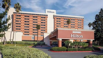 Un hôtel Hilton à l’architecture moderne, avec de nombreux étages et une entrée paysagée et bien entretenue.