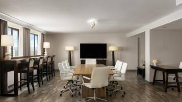 A conference room with a large table, white chairs, a flat-screen TV, and lamps.