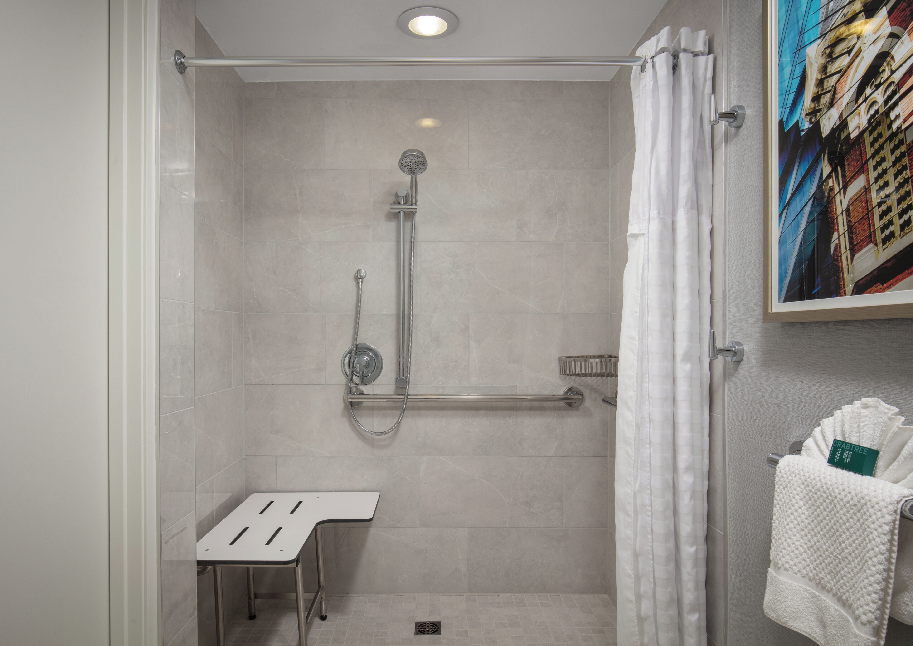 A modern shower with a handheld showerhead, a grab bar, and a small table.