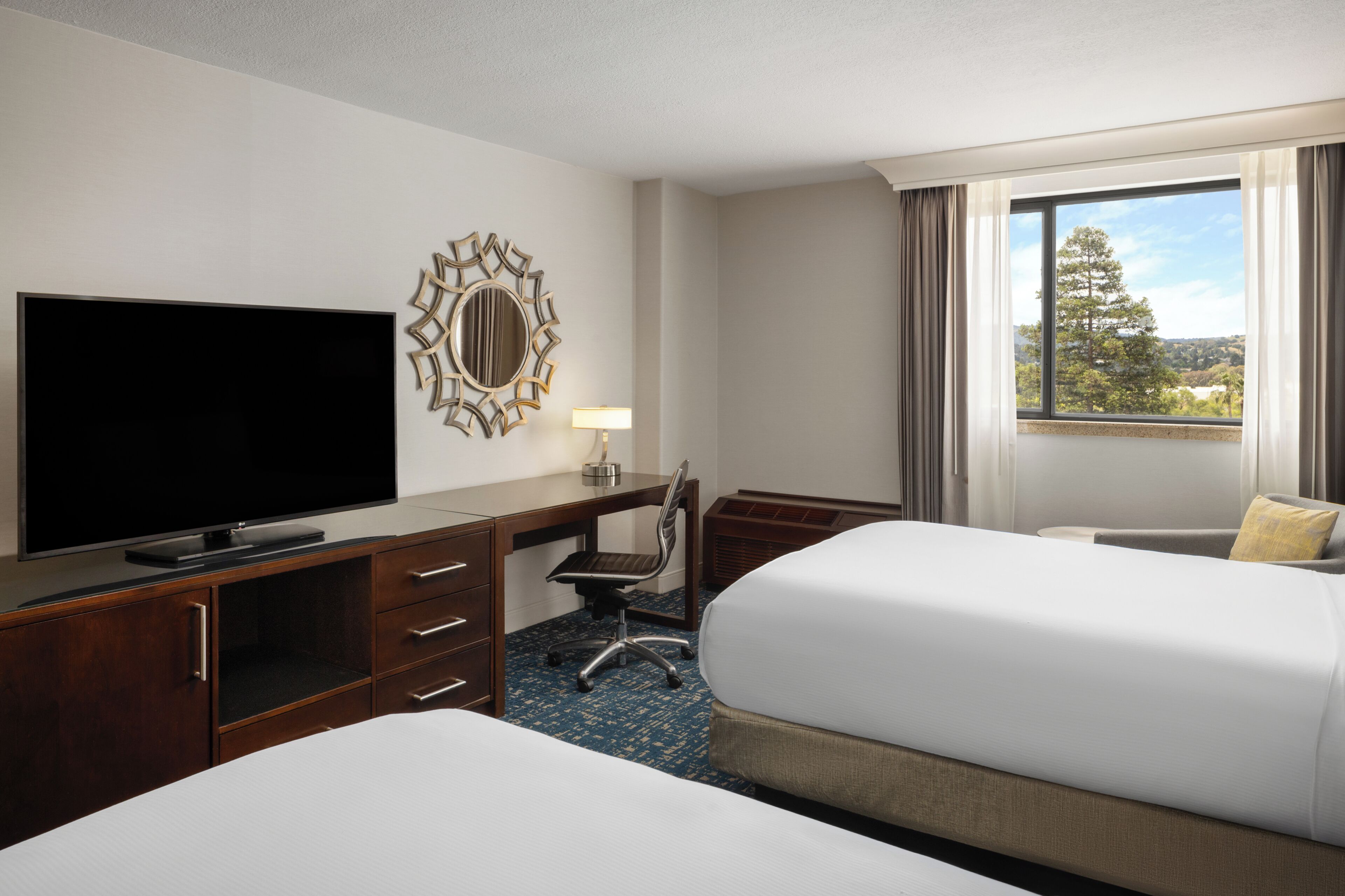 Een hotelkamer met televisie, bureau, stoel, twee bedden en een raam met uitzicht.