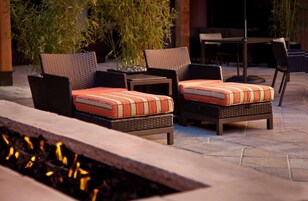 A patio area with wicker furniture, including two chairs and a small table, surrounded by potted plants.