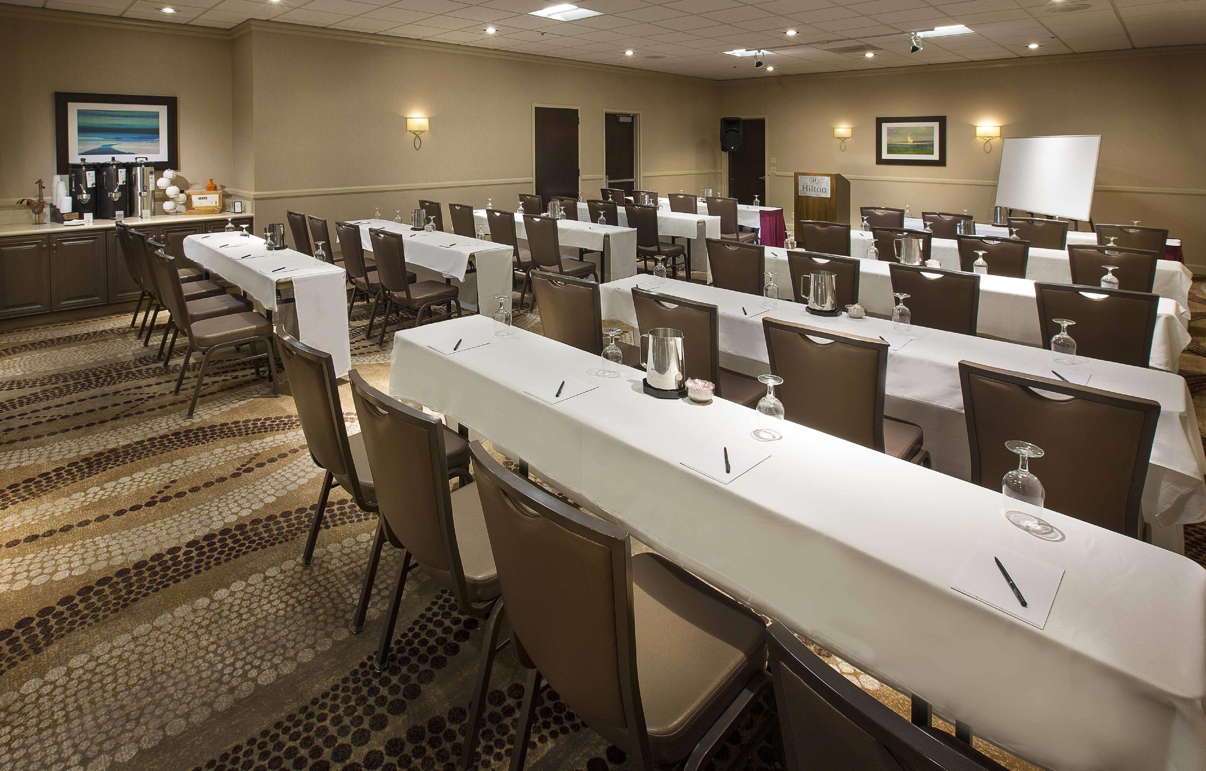 Un salón de conferencias con varias mesas, sillas y un escenario con un atril.