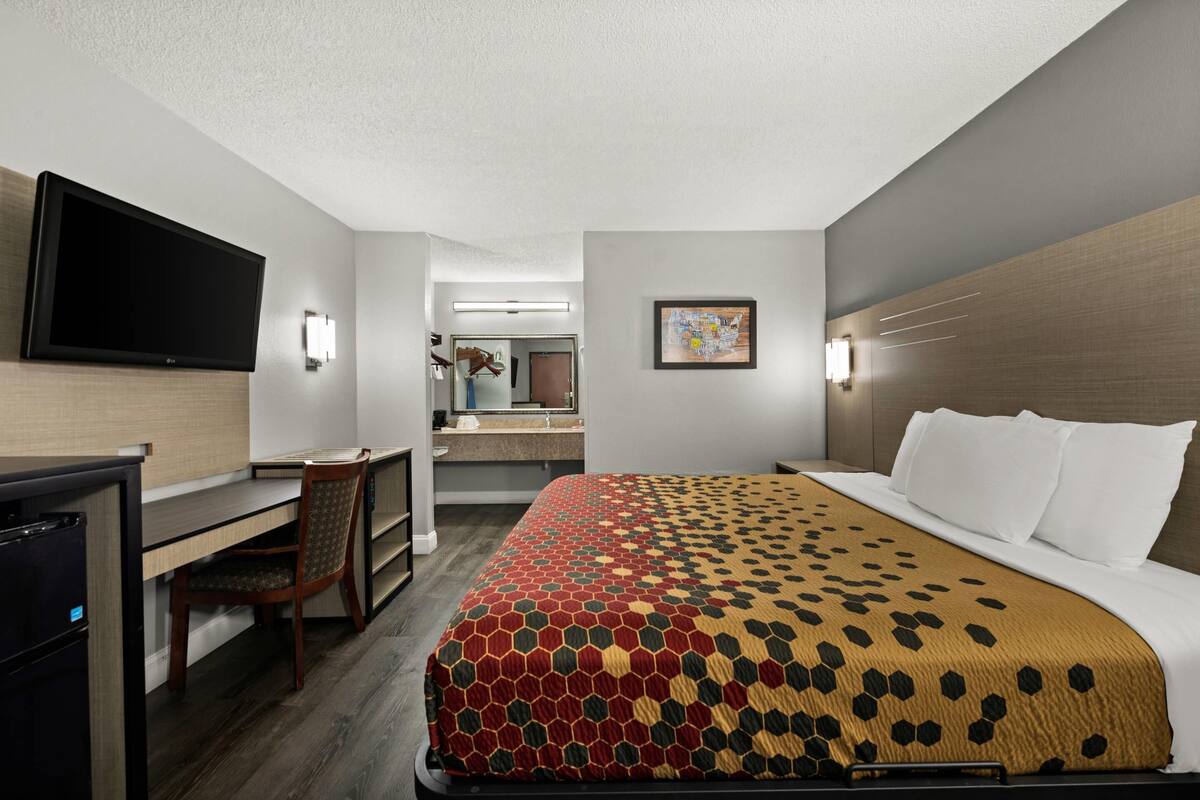 Une chambre d’hôtel avec un lit, un bureau, une chaise, une télévision, et une salle de bain visible au fond.