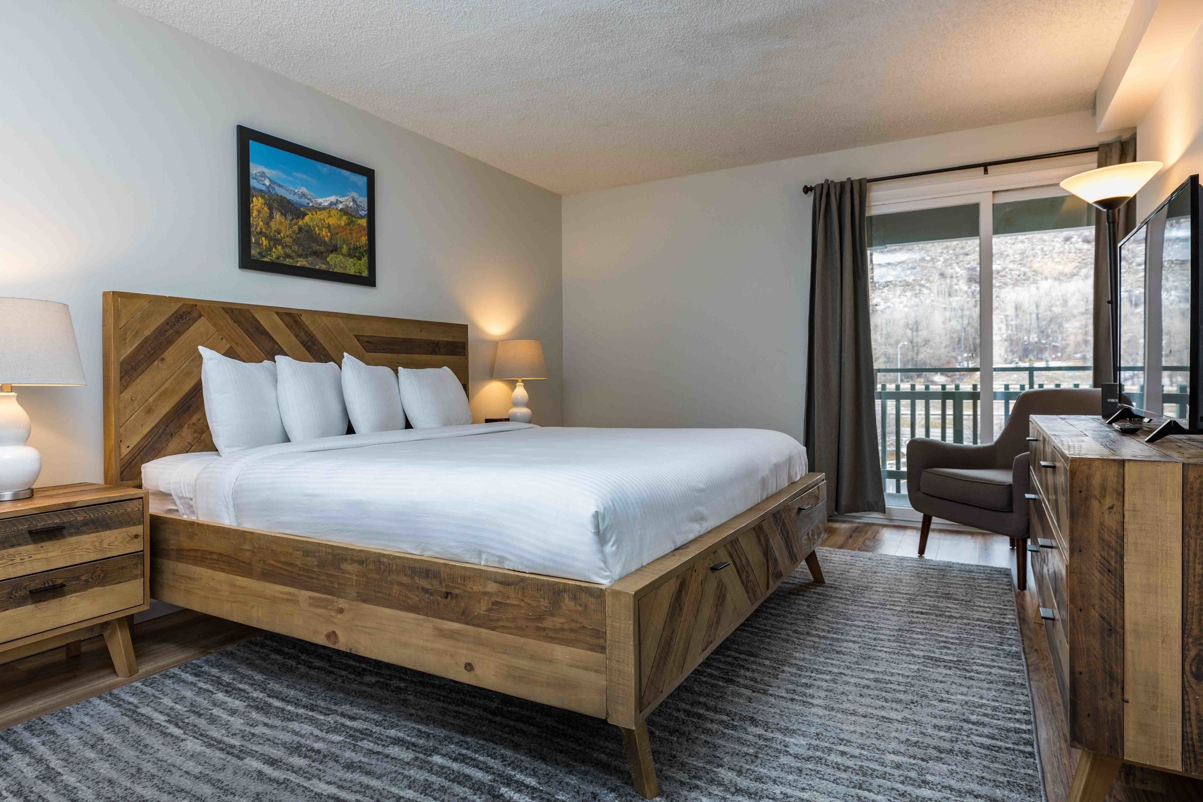 A bedroom with a wooden bed, bedside tables, a dresser, and a balcony with a view.
