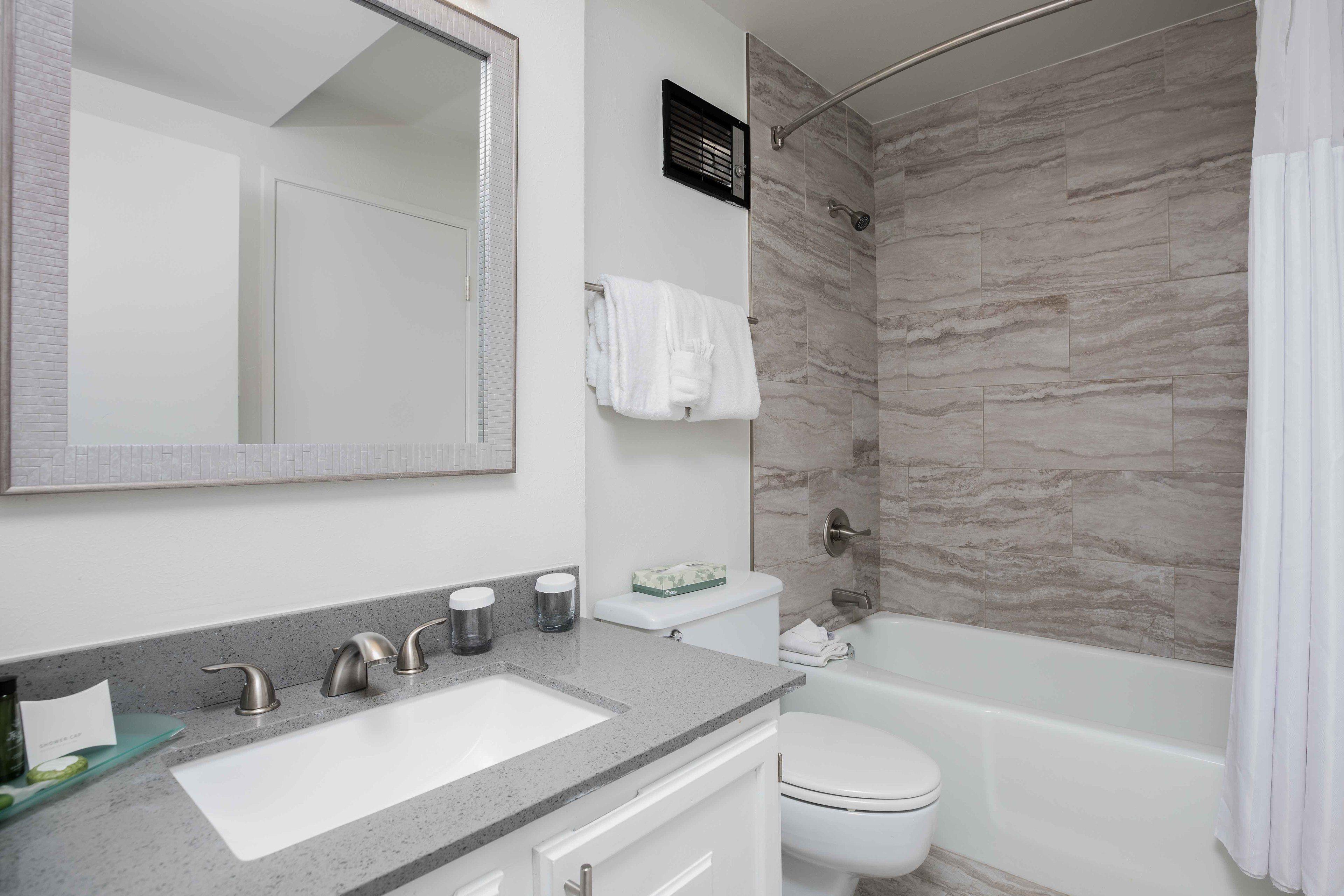 A modern bathroom with a large mirror, a sink, a toilet, and a shower area.