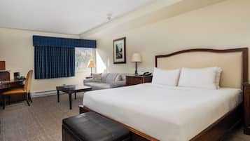 A hotel room with a large bed, a desk, a chair, a sofa, and a window with blue curtains.